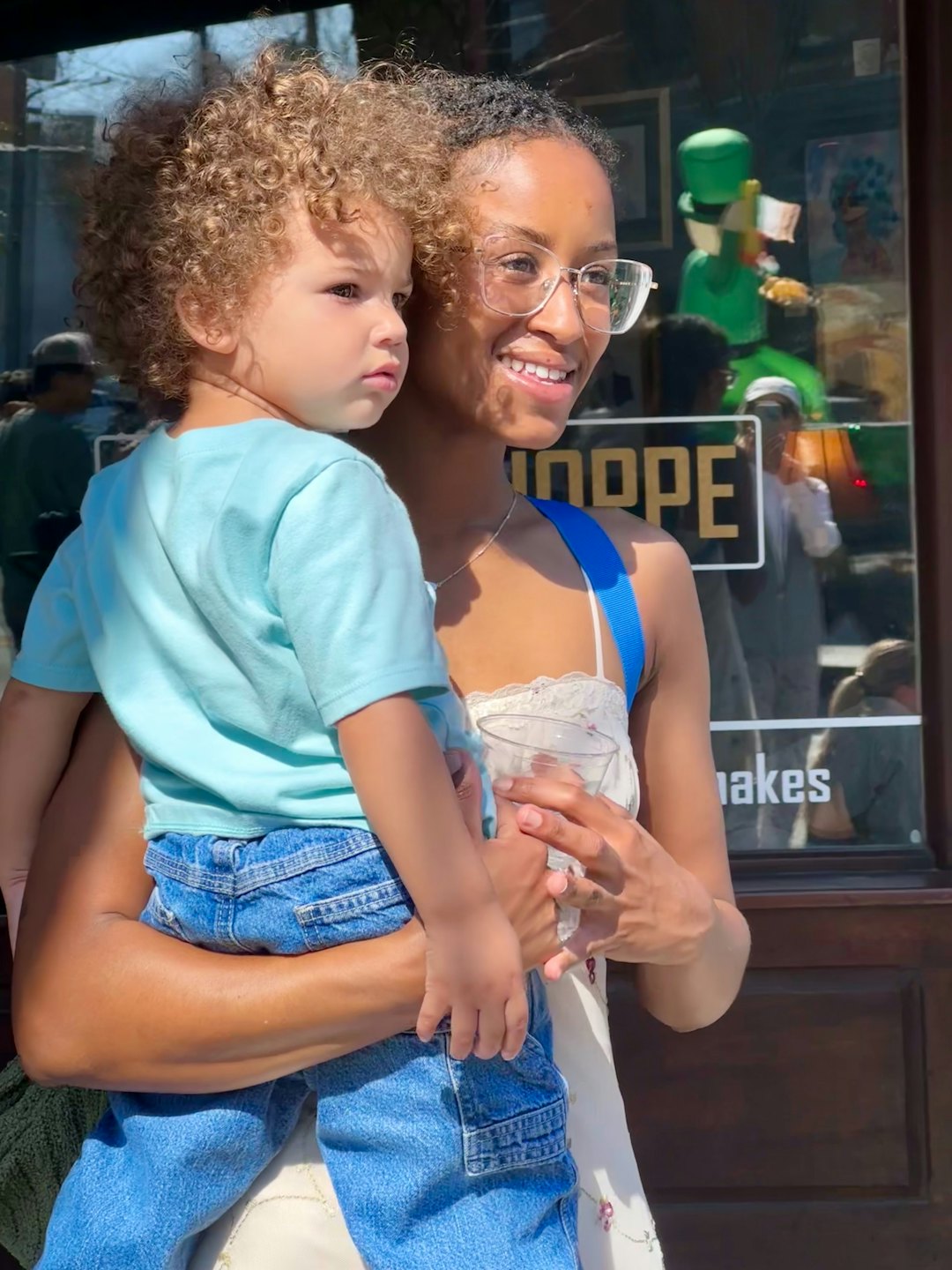 Mujer con gafas sostiene a un niño pequeño frente a un escaparate.