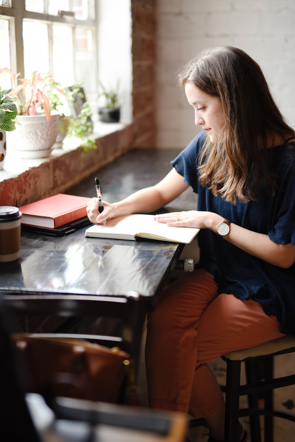 Mujer escribiendo en una libreta sobre una mesa de madera con plantas.